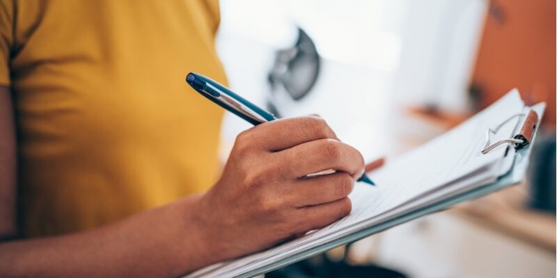 Image of person filling out a survey on a clipboard.