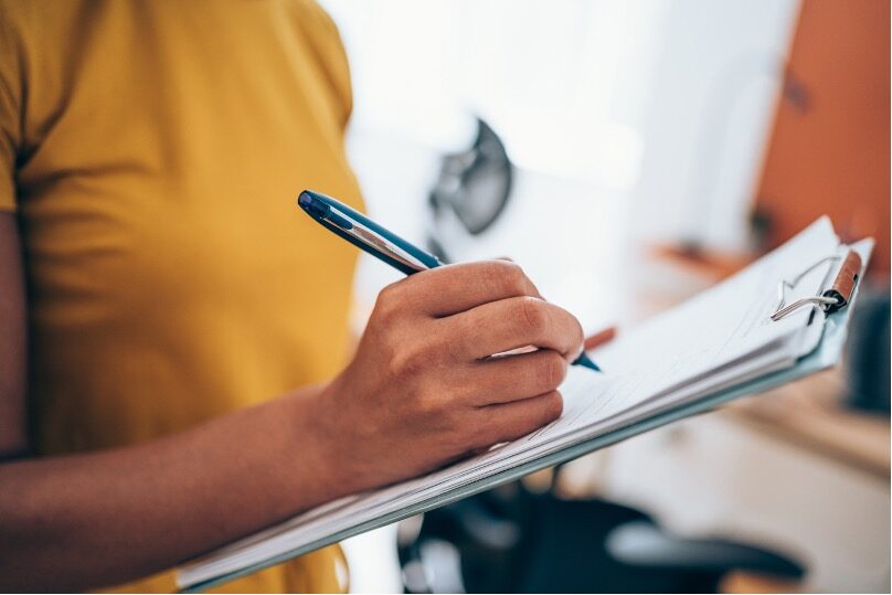 Image of person filling out a survey on a clipboard.